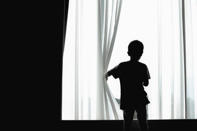 Rear view of boy standing by window at home