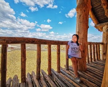 Portrait of woman standing on railing against sky