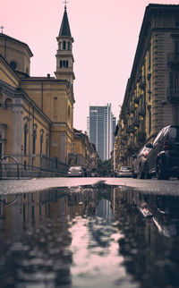 Reflection of buildings in street muddy against clear sky