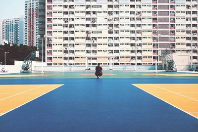 Rear view of man crouching at basket ball field against apartment building