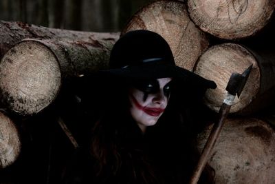 Portrait of woman in zombie make-up with axe against logs