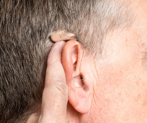 Close-up of senior man holding hearing aid against beige background