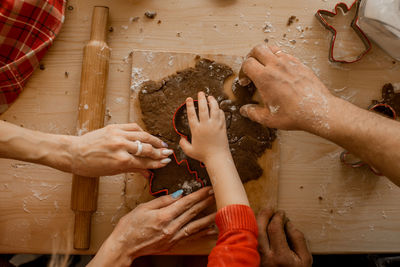 Top view of kid's and parents hands making christmas cookies or ginger bread in cozy kitchen 