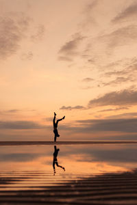 Silhouette man with arms raised against sky during sunset