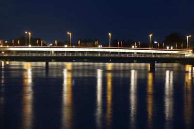 Illuminated buildings by river against sky at night