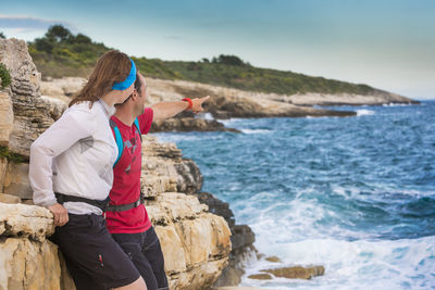 Man pointing by woman standing on rocky shore