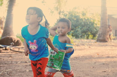 Siblings holding container while playing on ground