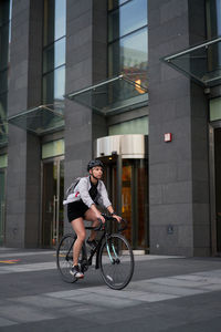 Man riding bicycle on street against building in city