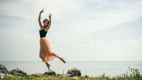 Woman dancing at beach against sky