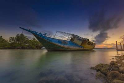 Fishing boat moored on sea against sky during sunset