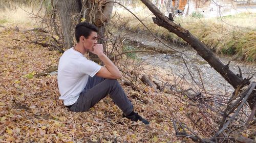 Thoughtful man sitting on dry leaves by stream at forest