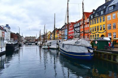 Sailboats moored on canal by buildings against sky in city