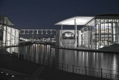 Illuminated bridge over river in city against clear sky at night