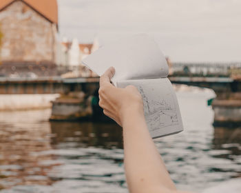 Cropped hand holding book by canal