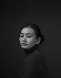 Side view of thoughtful young woman looking away while standing against black background