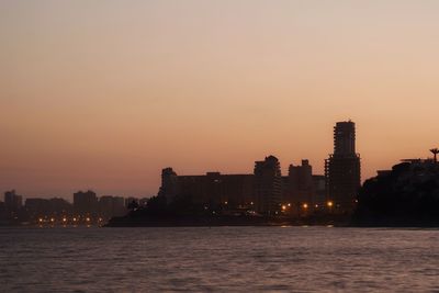 Sea by buildings against sky during sunset