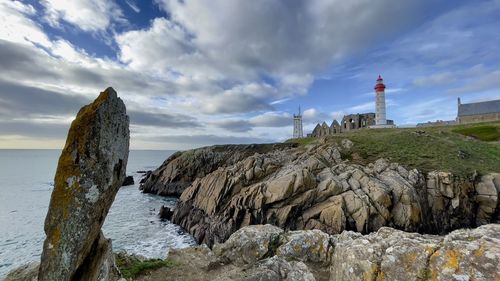 Lighthouse on rocks by sea against sky