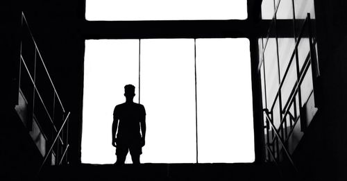 Silhouette man standing by window against clear sky