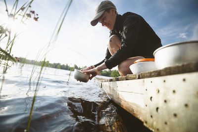 Smiling woman washing pots in lake