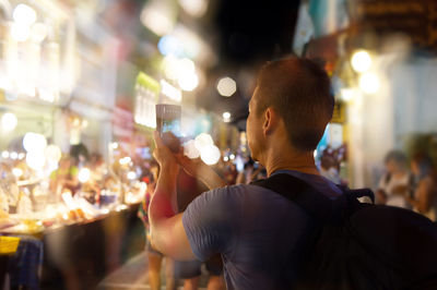 Man photographing while standing on street in illuminated city at night