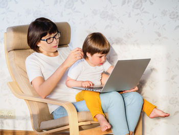 Mother and her boy sit together with laptop. woman tries to remote work, kid is asking for cartoons.