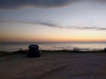 Car on beach against sky during sunset