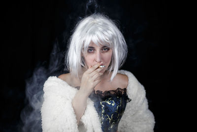 Portrait of female model smoking cigarette against black background