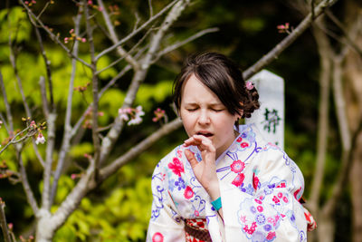 Woman in kimono making face against trees
