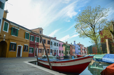 Boats moored on canal by buildings against sky