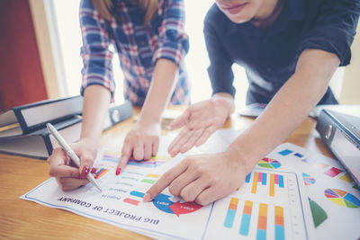 Midsection of business people pointing at graph on table