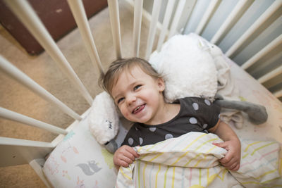 High angle of cute toddler girl smiling in her bed