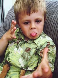 Boy sticking out tongue while sitting on sofa at home