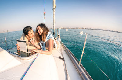 Couple lying on boat in sea against clear sky during sunset