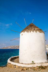Traditional windmill by sea against blue sky
