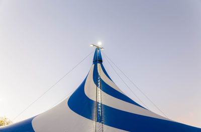 Low angle view of illuminated lights on striped circus tent against sky