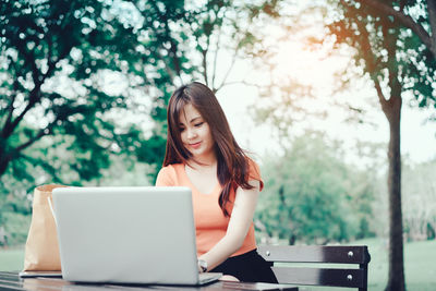 Young woman using phone while sitting on tree