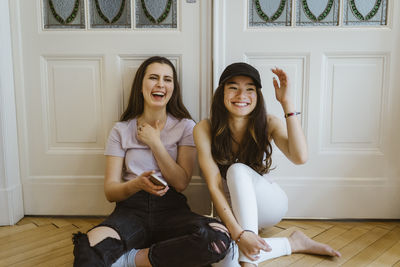 Happy young women sitting against white door at home