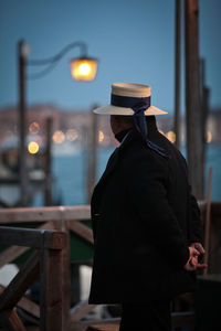 Rear view of man standing by canal at dusk