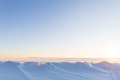 Winter landscape, snowy hills, frozen sea, lots of blue sky, sunrise or sunset. 