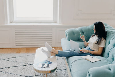 Full length of woman using smart phone while working at home