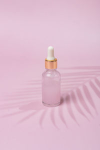 Glass cosmetic bottle dropper with beuty oil or serum for skin care on pink background. natural skin