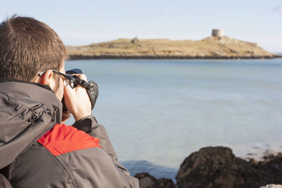 Rear view of man photographing sea against sky