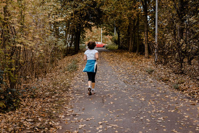 Rear view of woman running on leaves covered road