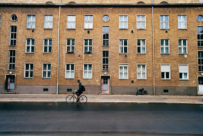 Person riding bicycle on road by building