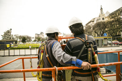 Rear view of men standing against railing in city