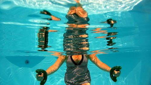 Midsection of young woman holding weights swimming in pool