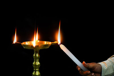 Cropped hand igniting candle against black background