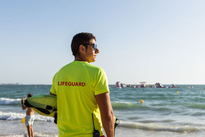 Back view of male lifeguard in shorts and t shirt and maintaining safety on sandy seashore