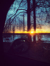 Silhouette bare trees by lake against sky during sunset