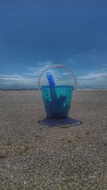 Close-up of blue container on sand against sky